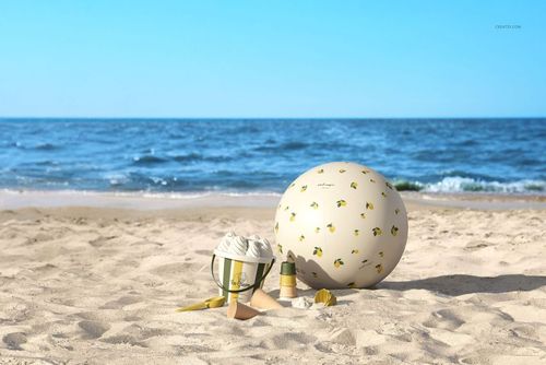 Beach ball mockup featuring a white ball with small yellow designs on sand, with sea waves and horizon behind.