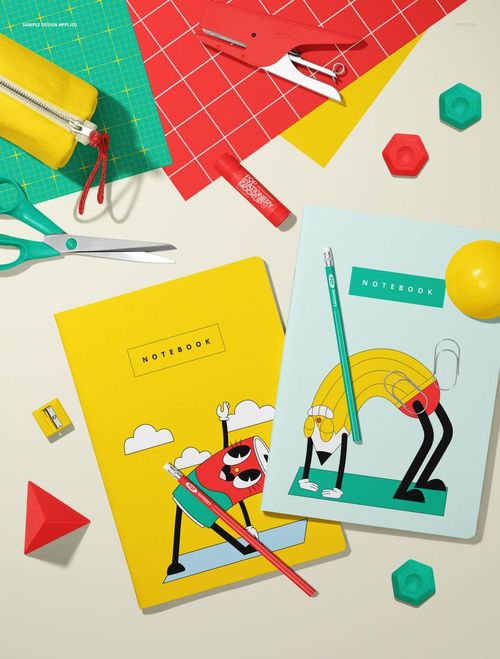 Stationery mockup with two illustrated A4 notebooks, pencils, eraser, and various desk accessories arranged on a light surface.