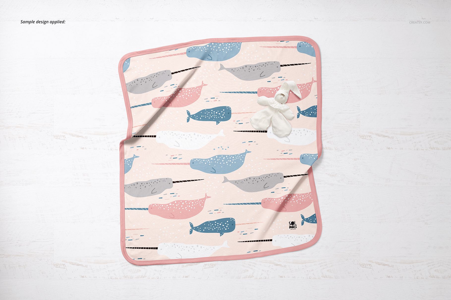 Top view of a cotton baby blanket mockup featuring colorful whales and pink trim, displayed with white socks.