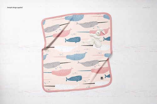Top view of a cotton baby blanket mockup featuring colorful whales and pink trim, displayed with white socks.