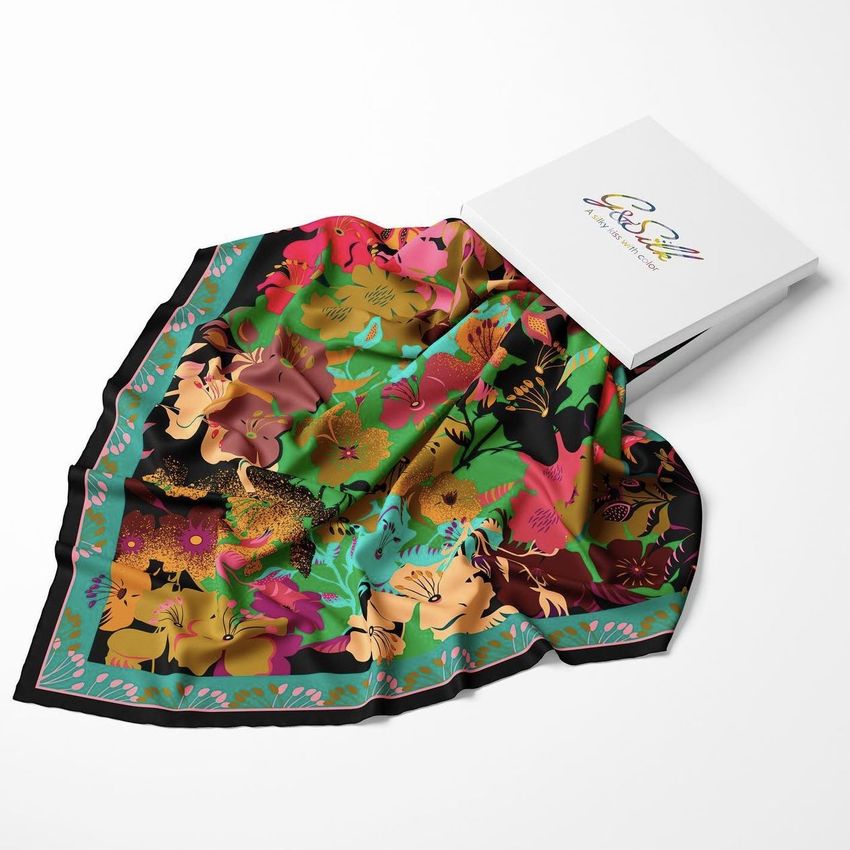 Twill silk scarf mockup featuring a vibrant floral pattern in red, green, and yellow tones, displayed next to a white box on a white surface.