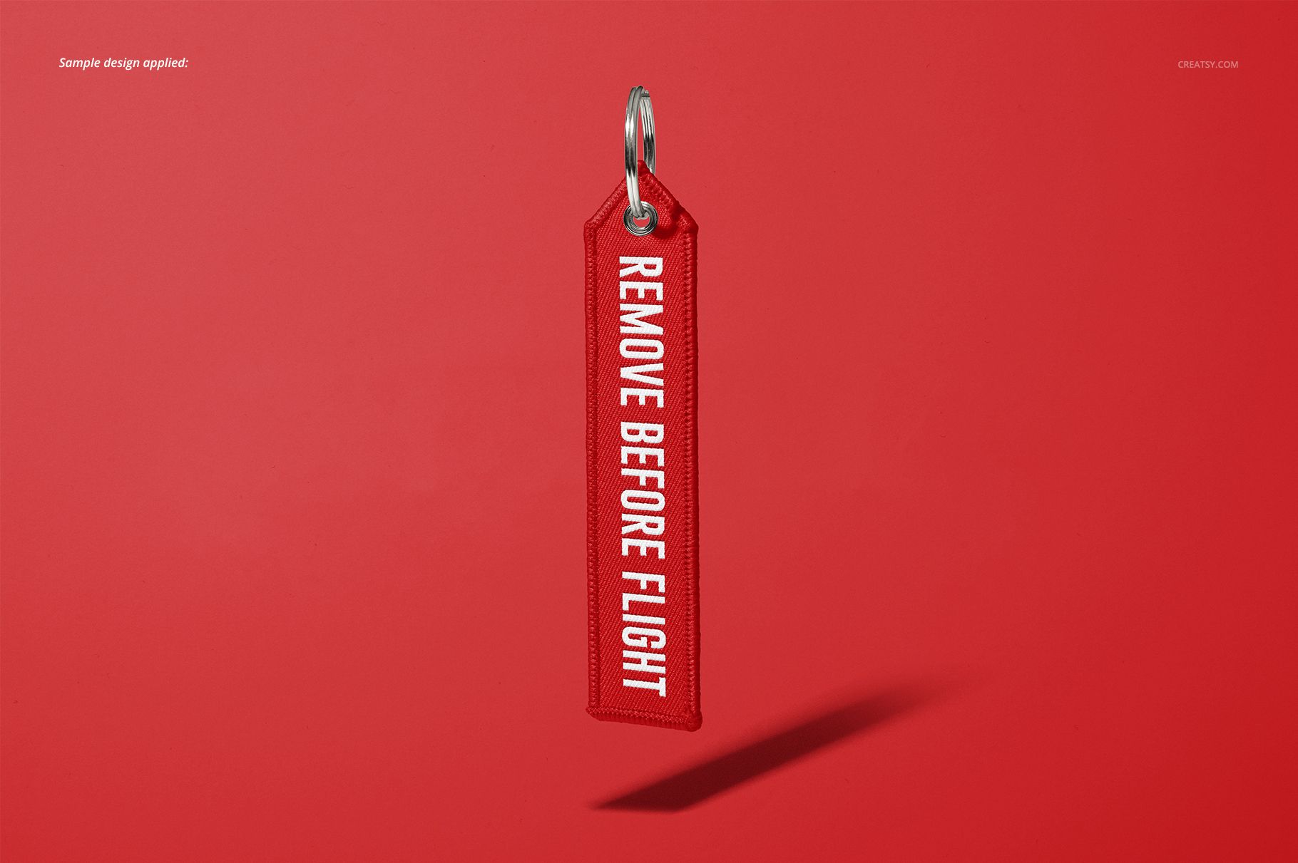 Mockup of a red 'Remove Before Flight' keychain, showing stitched edges and metal ring, centered on a plain red surface.