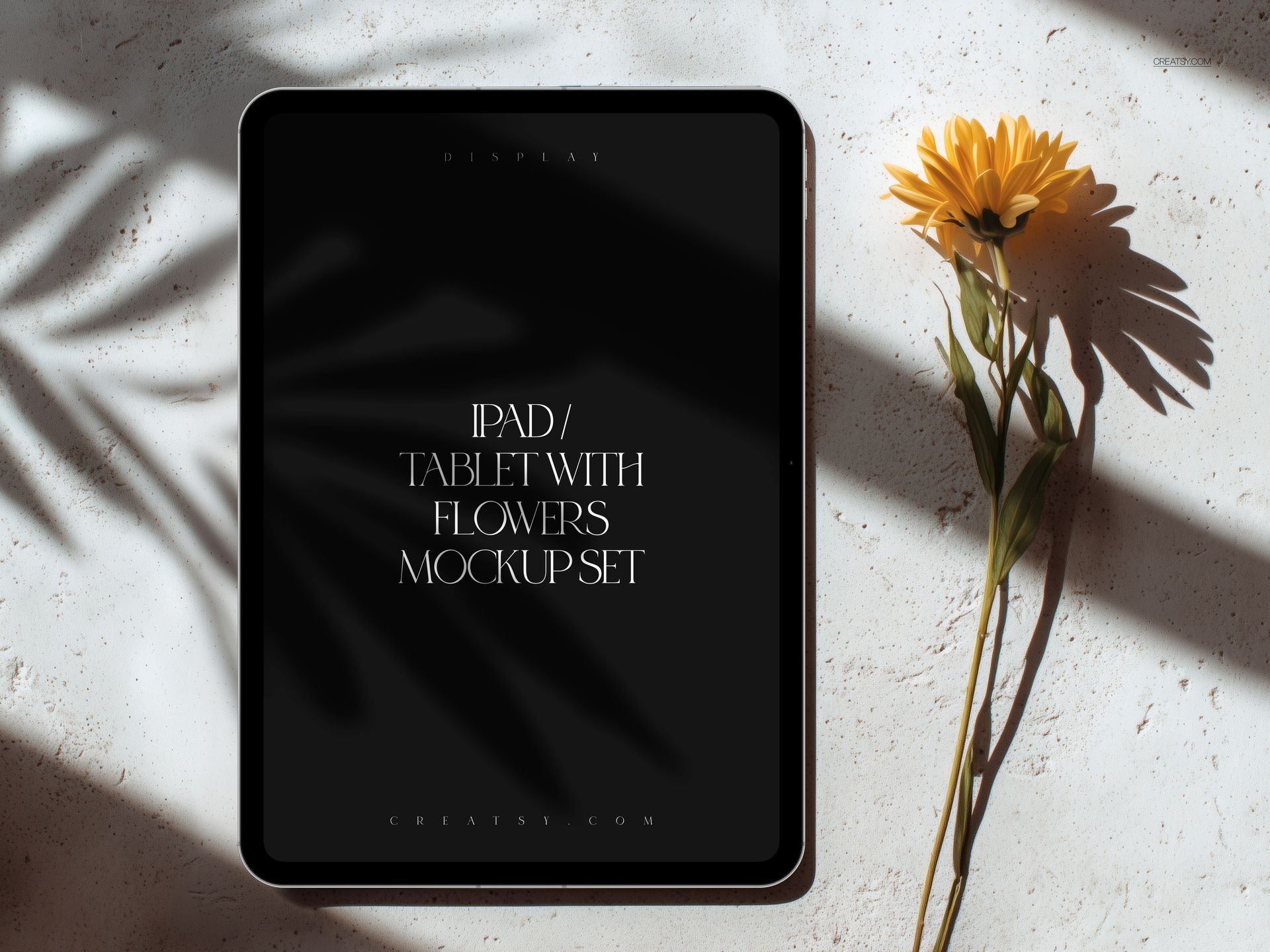 Front view of an iPad Pro mockup with a dark screen, placed on a light surface next to a yellow flower.