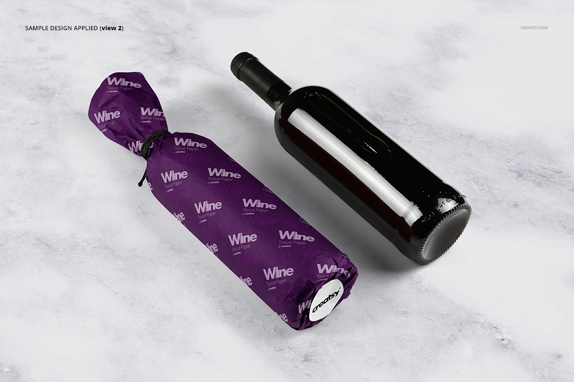 PSD mockup showing a wine bottle covered in purple tissue paper with white lettering, beside a plain bottle on marble.