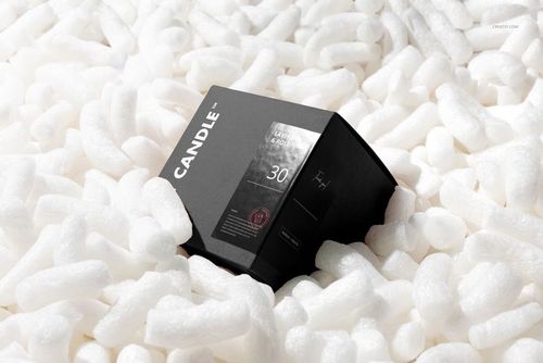 Square box with a black label resting among white packaging peanuts, shown from a front angle in a mockup scene.