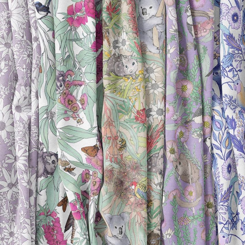 Creased fabrics mockup showing several draped textile panels with colorful floral and animal patterns in pastel and vivid tones.