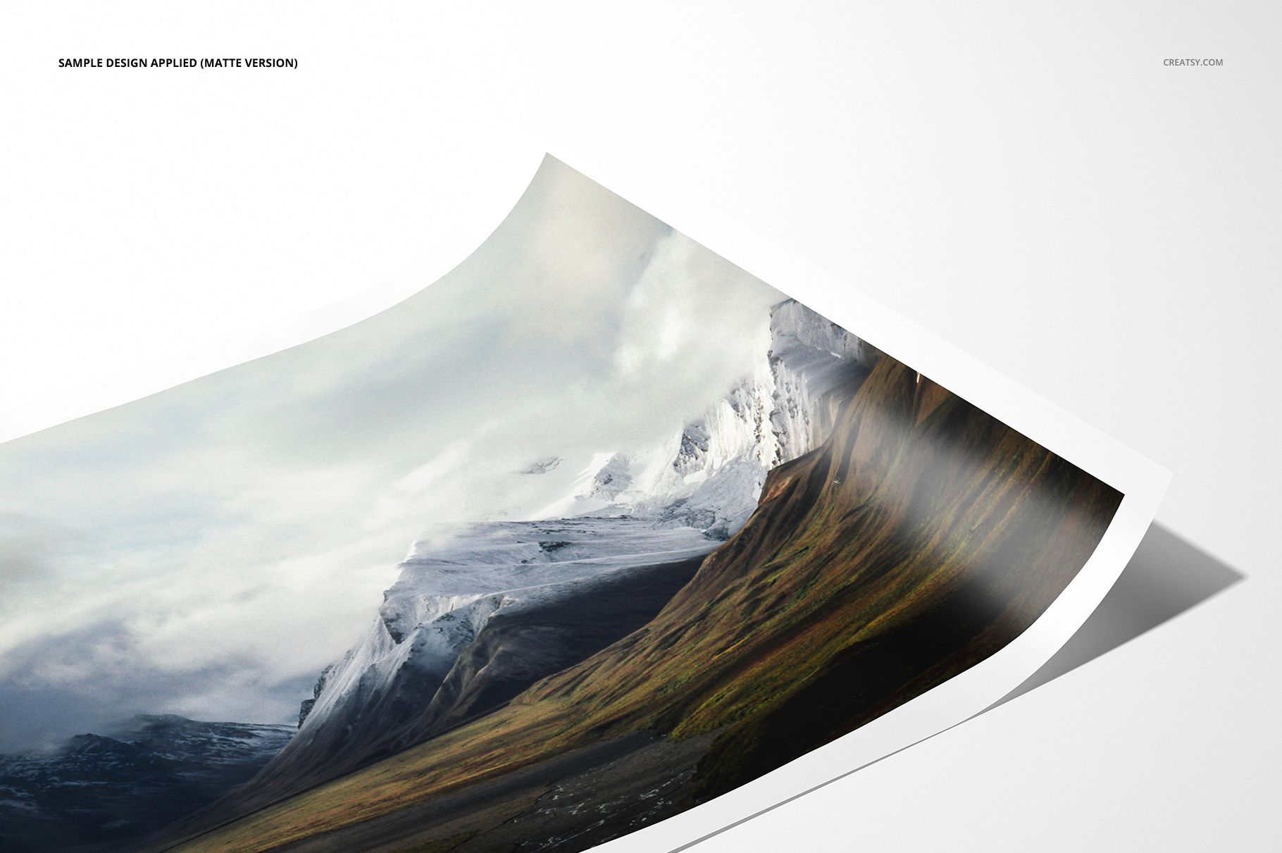Matte photo print mockup featuring a landscape image of snowy mountains and green hills, angled view on white background.