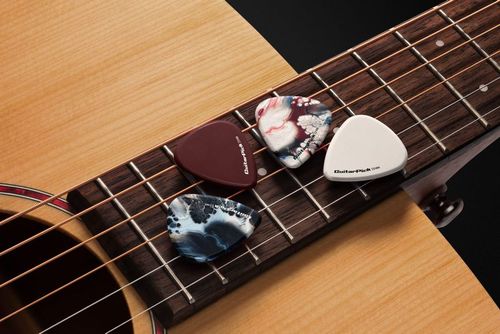 Assorted guitar picks placed across the strings and fretboard of a wooden acoustic guitar in a detailed mockup scene.