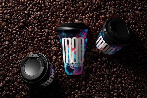 PSD mockup of paper cups with vibrant patterns and black lids displayed among scattered coffee beans, viewed from above.