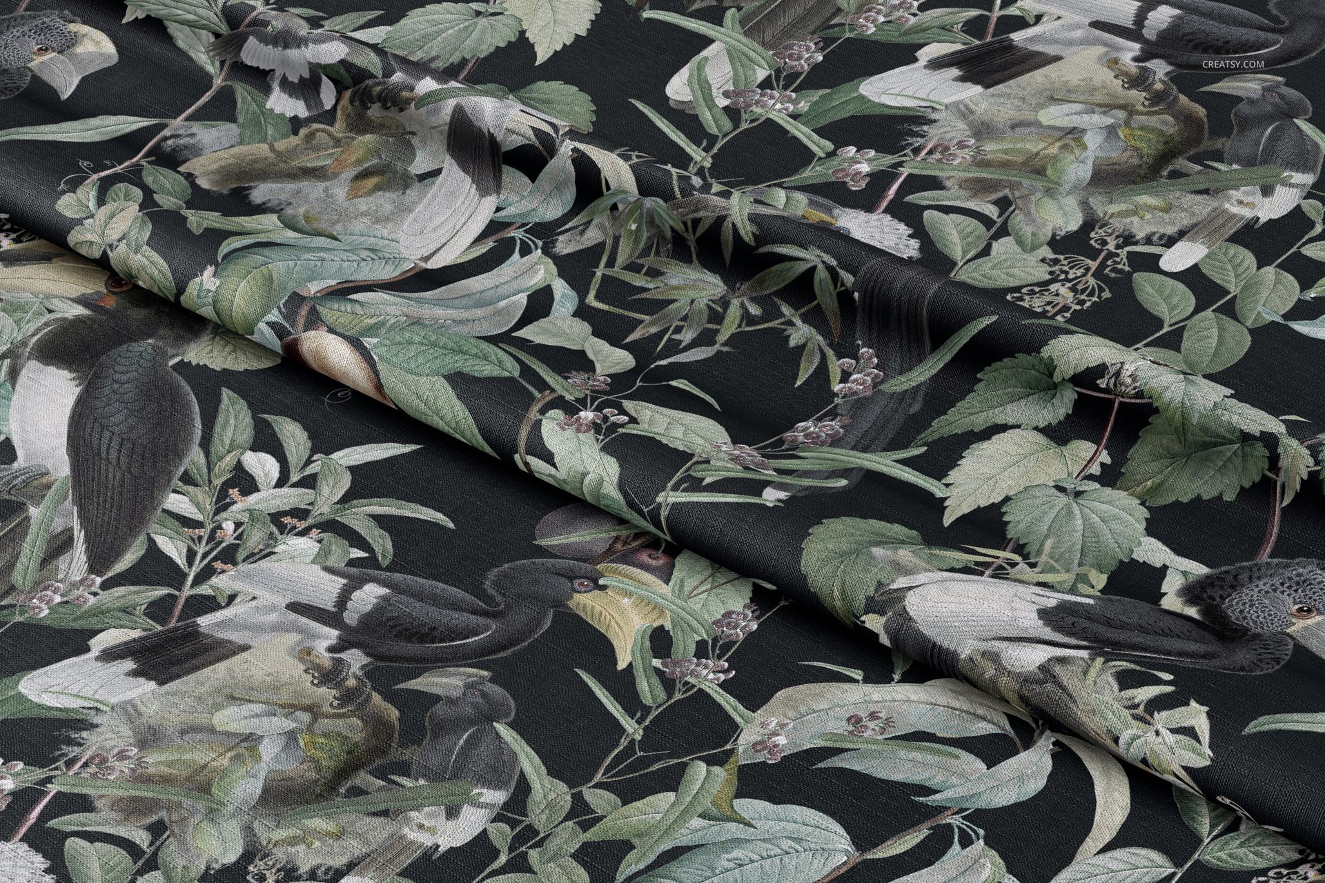 Folded tablecloth fabric mockup with illustrated birds and green foliage on a dark background, viewed from above.