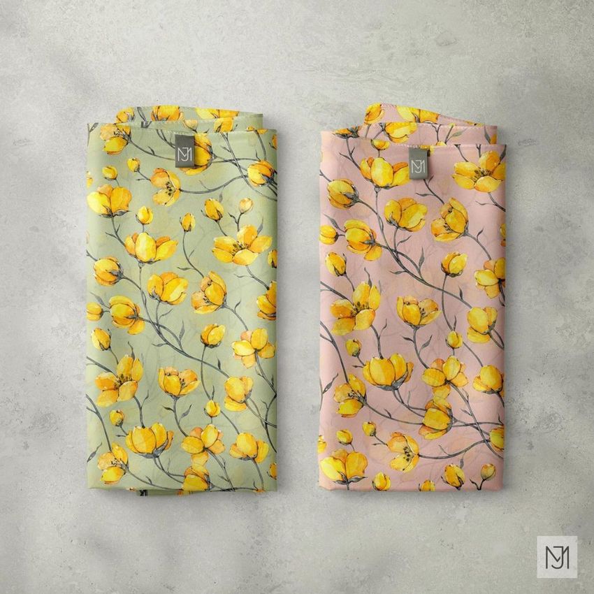 Silk scarf mockup showing two folded scarves, one green and one pink, both with yellow floral patterns and small labels on a gray surface.