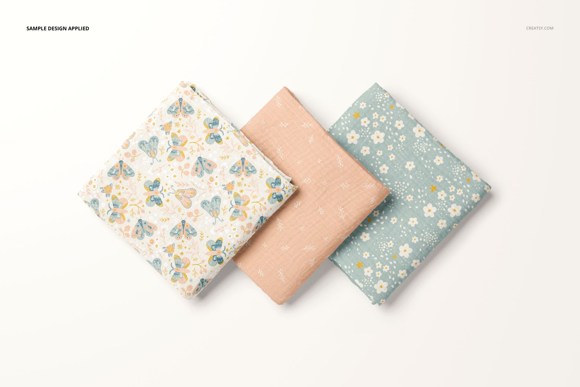 Crinkle muslin swaddle blanket PSD mockup showing three folded blankets with distinct patterns and gentle hues.