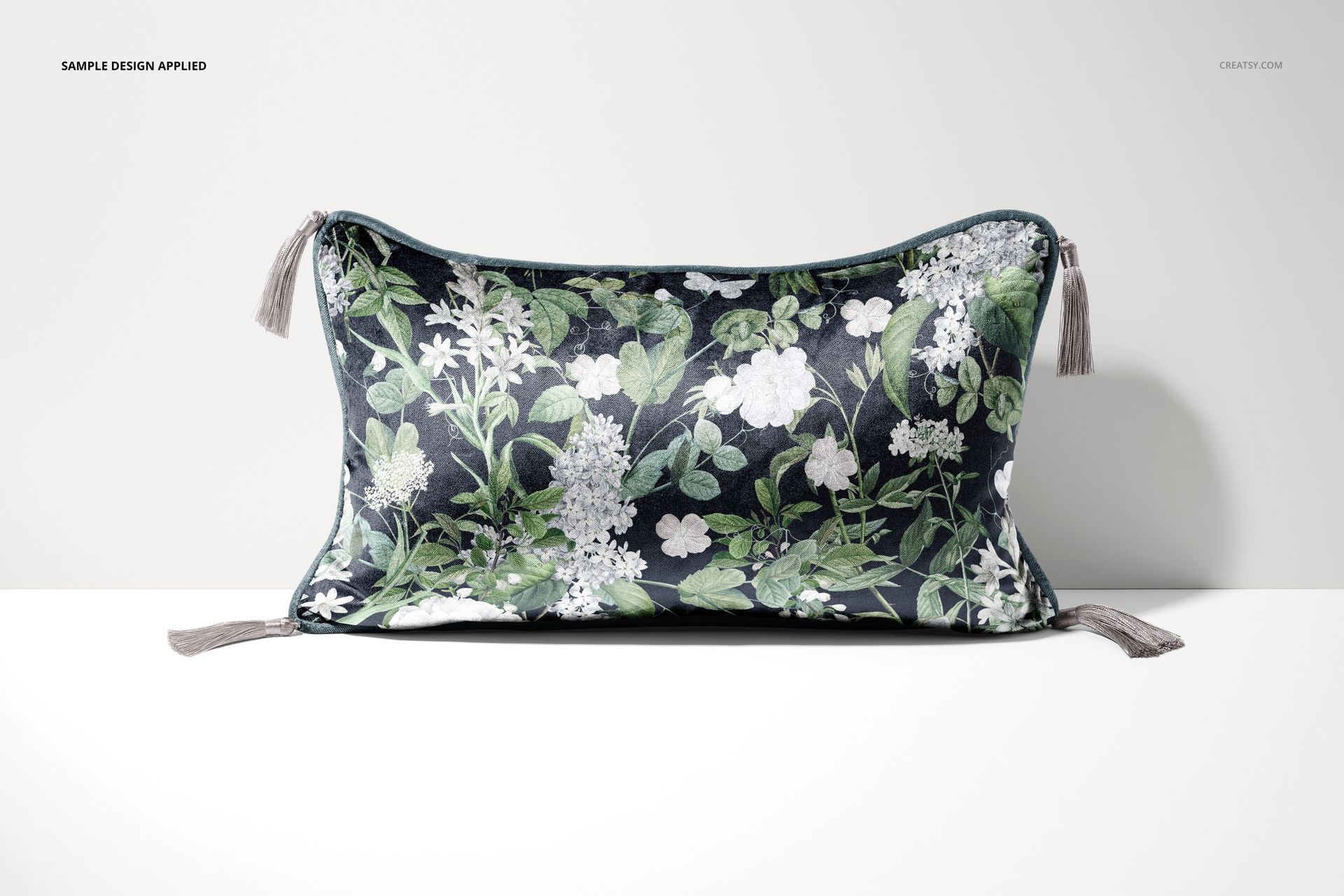 PSD mockup showing a rectangular cushion with tassels, botanical design in green and white, displayed on a plain surface.