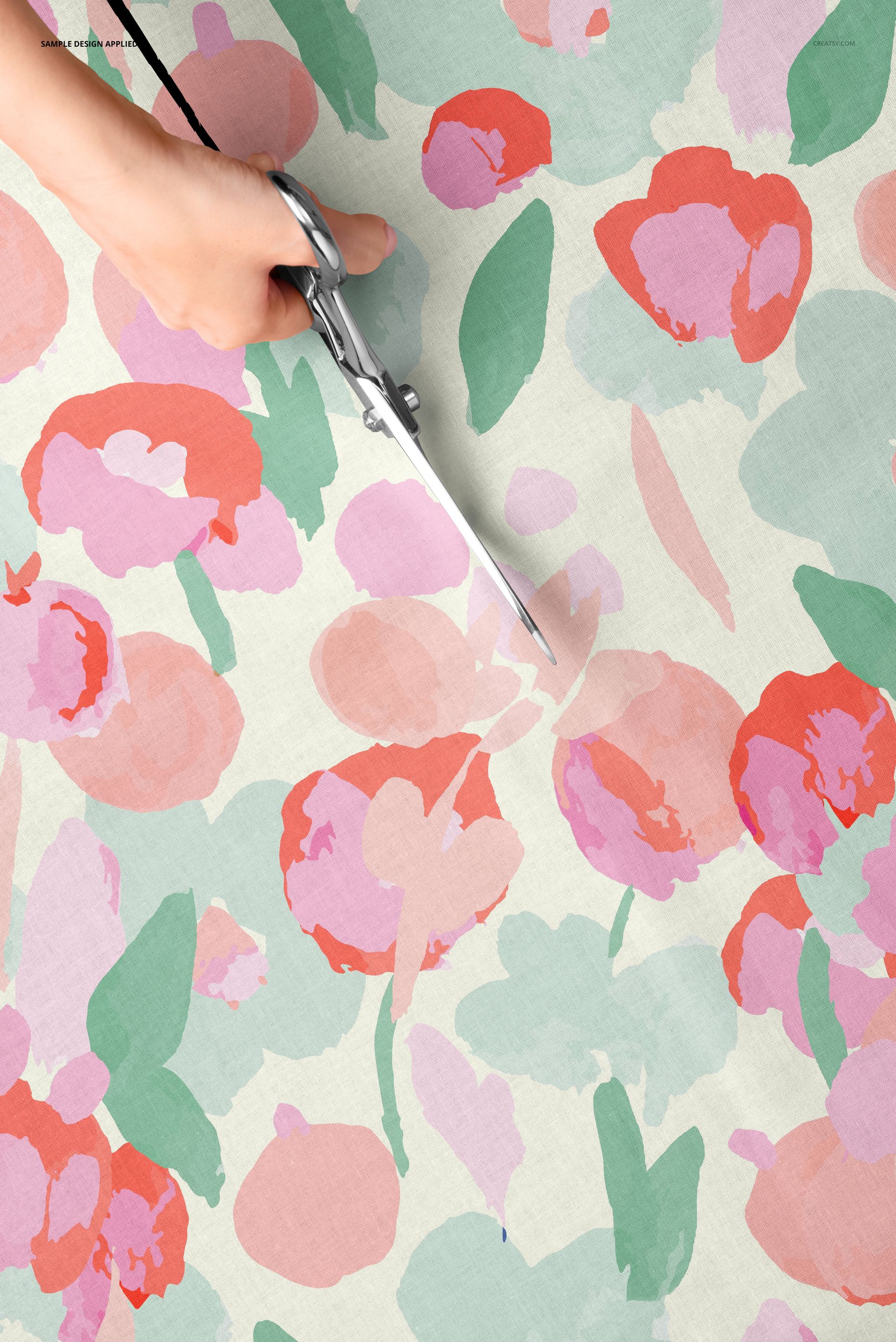 Close-up view of a hand using scissors to cut cotton fabric with a colorful floral pattern, top perspective.