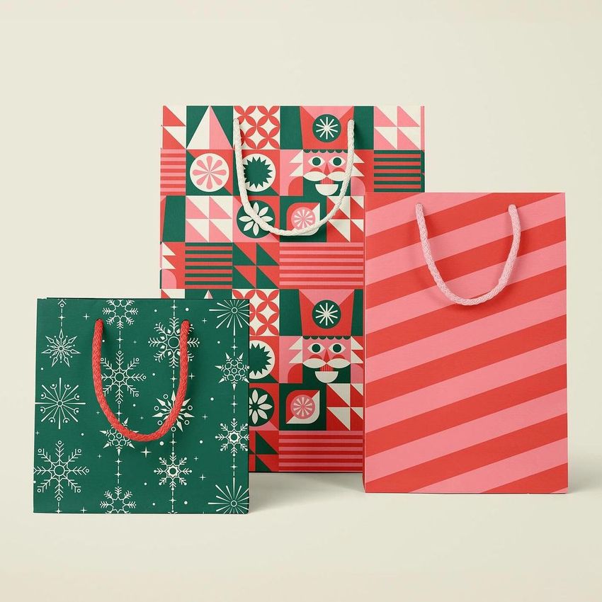 Paper bags mockup featuring three bags with festive designs, including geometric patterns, snowflakes, and diagonal stripes on a neutral background.
