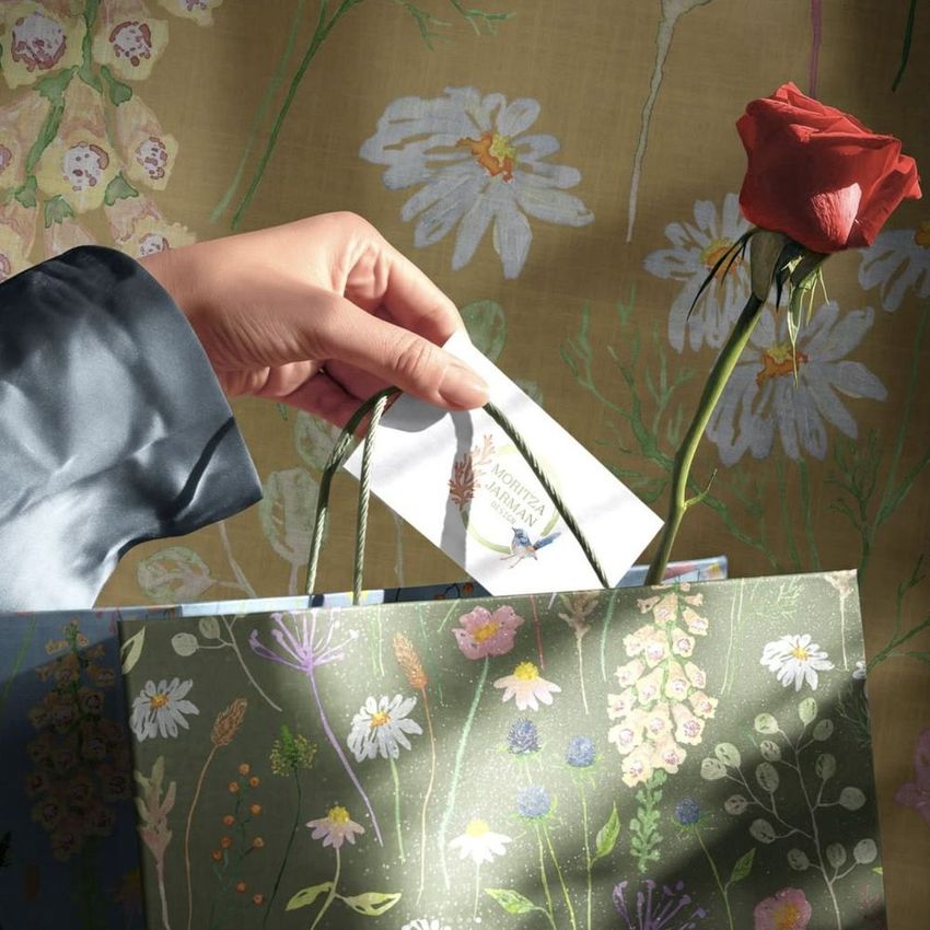 Floral-themed gift packaging mockup showing a card being added to a bag with botanical patterns and a red rose on a soft background.