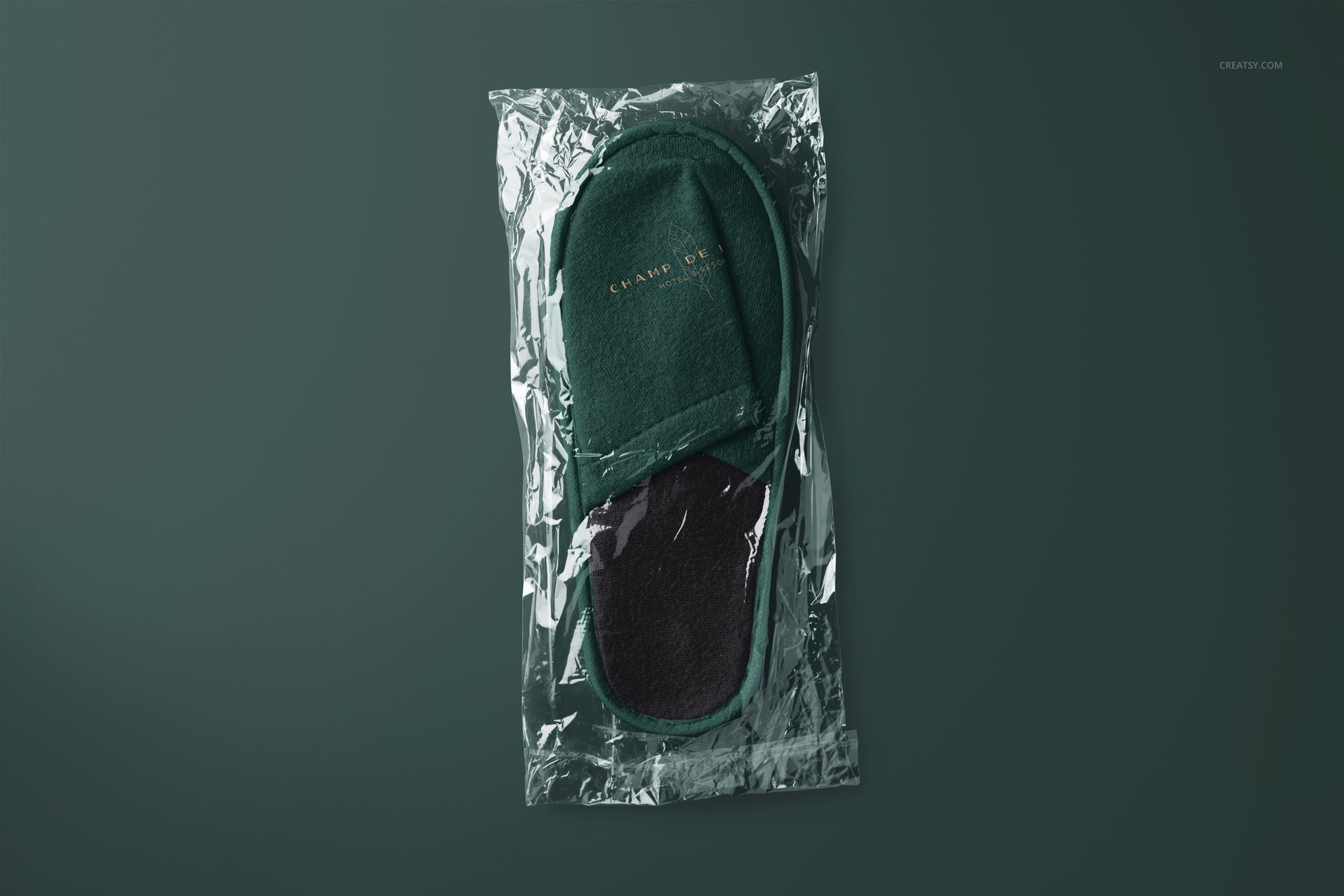 Dark green slippers mockup set in clear plastic wrap, viewed from above against a solid dark background.