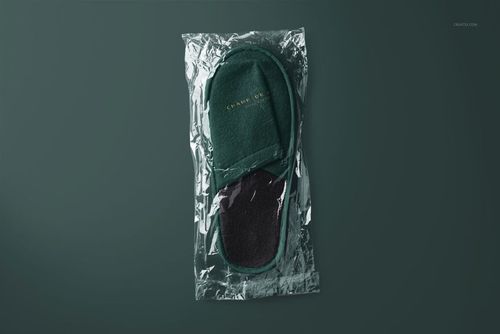 Dark green slippers mockup set in clear plastic wrap, viewed from above against a solid dark background.