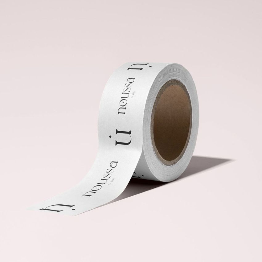 Packaging tape mockup featuring a single roll of white tape with black serif text, displayed on a light pink background.