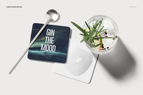 PSD mockup displaying square coasters with modern artwork, accompanied by a clear glass and metallic spoon.
