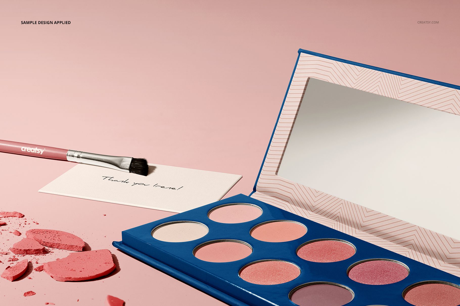 Eyeshadow palette mockup set featuring a blue case, assorted pink shades, mirror, and brush on a pink background.