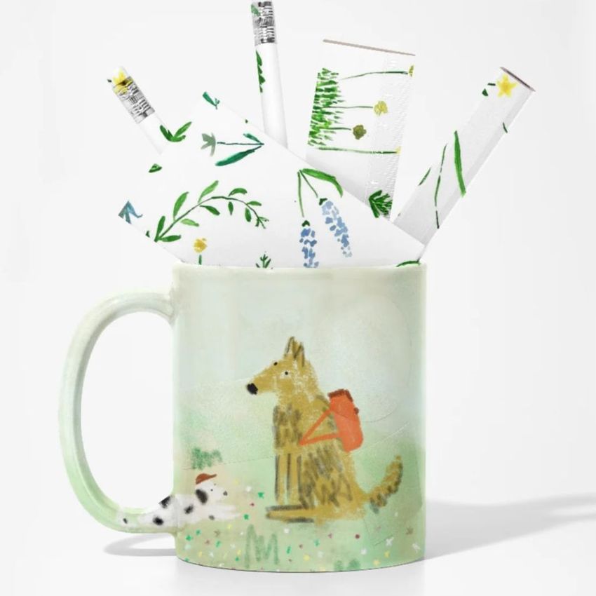 Mug mockup featuring a watercolor-style illustration of a dog with a backpack, holding rolled stationery with floral patterns.
