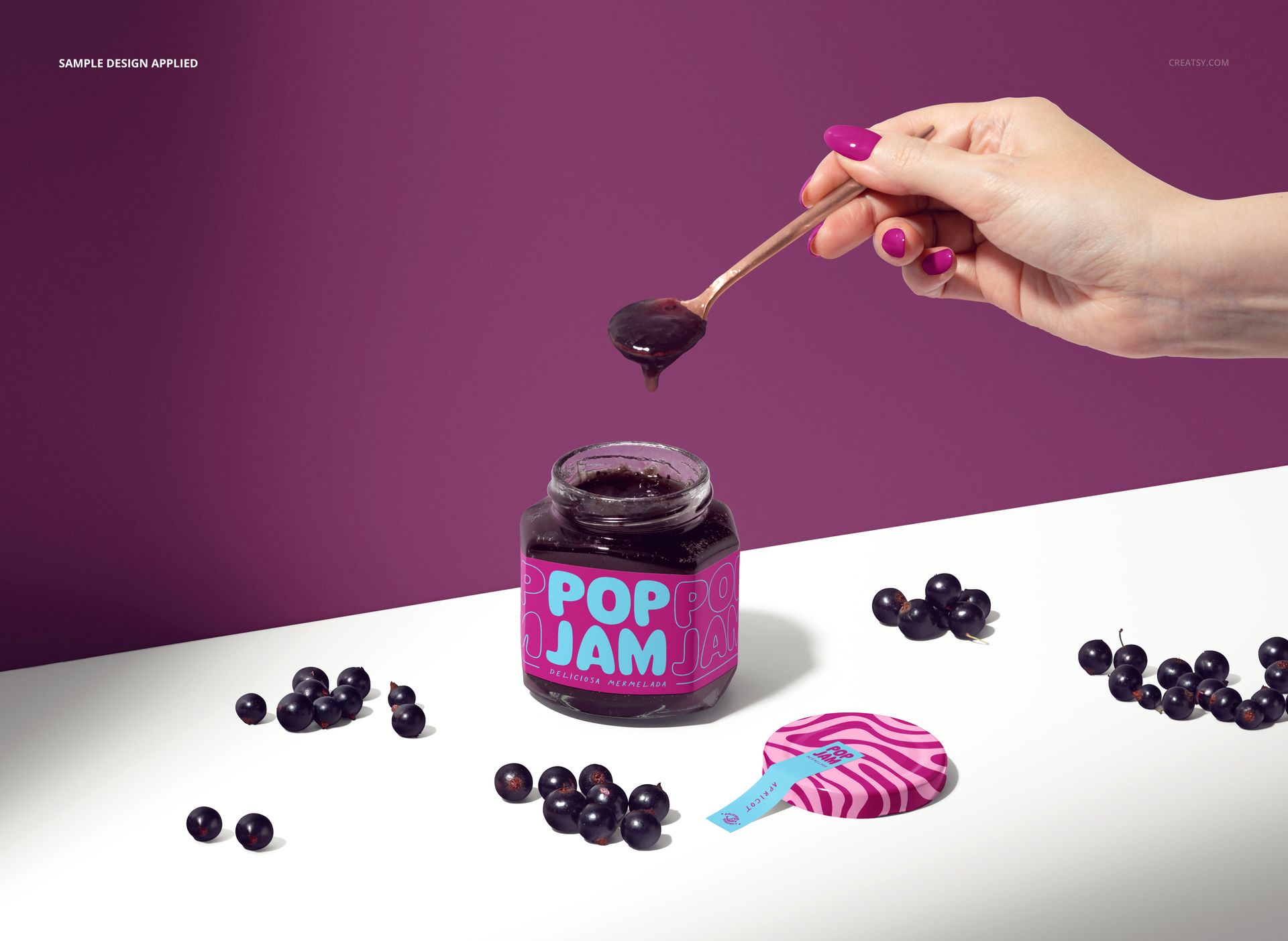 PSD mockup showing a glass jam jar with purple jam, a spoon held above, and scattered blackcurrants on the table.