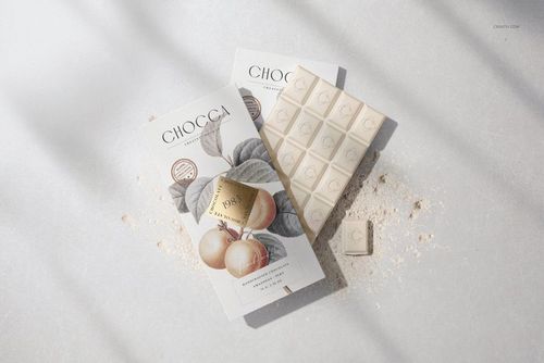 Front view of chocolate bar packaging mockup with botanical illustration, white chocolate bar and powder on light surface.