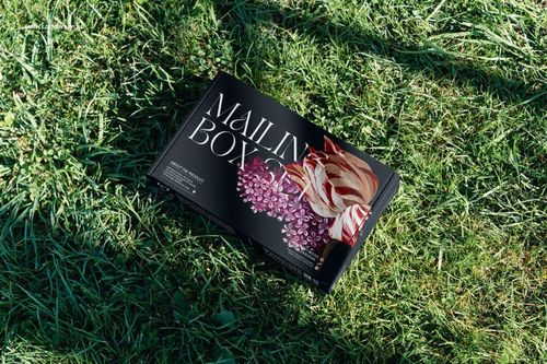 Mailing box mockup with dark background and colorful flower artwork placed outdoors on grassy ground.