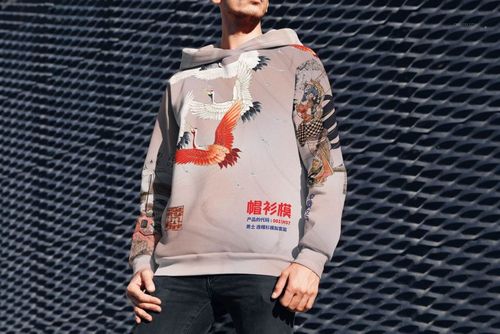 PSD mockup of oversized hoodie with colorful crane and graphic elements, modeled outside near a geometric background.