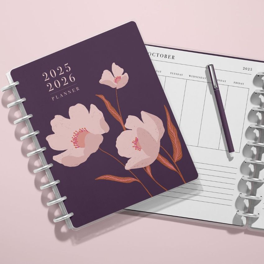Top view of two spiral planners on a light pink surface, one closed with a floral cover and one open to a calendar page.
