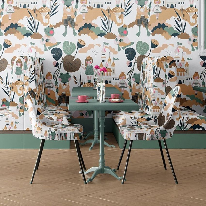 Cafe interior wallpaper mockup showing a whimsical frog prince pattern on the walls and chairs, with a table set for tea.