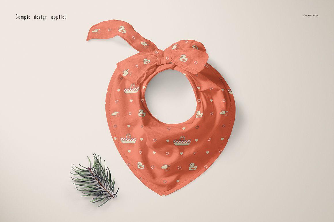 Coral baby bandana bib mockup featuring swan motifs and small geometric shapes, shown from above on a neutral background.