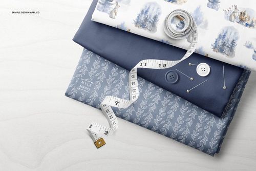 Folded fabrics mockup with blue and white textile layers, decorative patterns, and sewing props including buttons and tape.