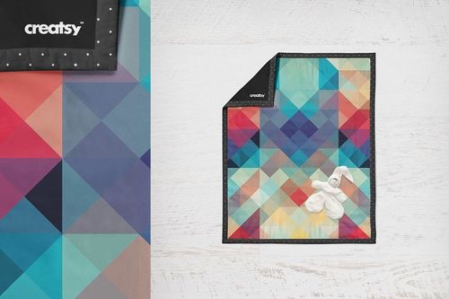 Baby quilt mockup featuring vibrant multicolor triangles, displayed flat with a small white plush bunny on top.