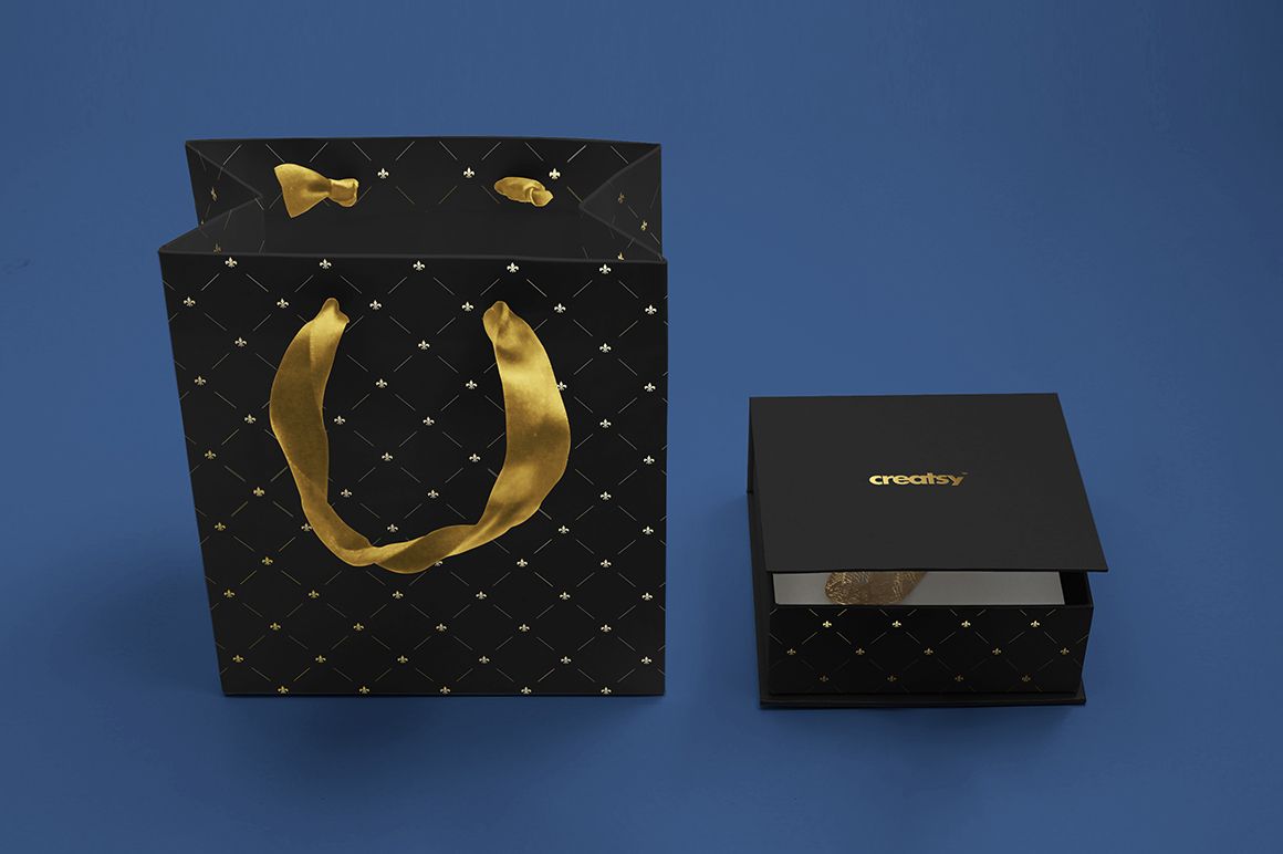 Jewelry box mockup set featuring a black box with gold accents and a coordinating gift bag on a blue background.