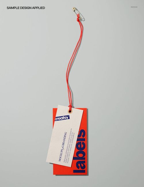 Clothing paper labels mockup featuring two rectangular tags, one red and one beige, attached with a red string and safety pin, shown from above.