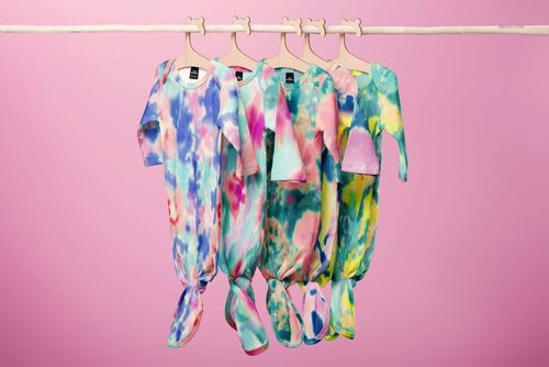 PSD mockup featuring baby ribbed knotted gowns and hats in assorted bright tie-dye patterns hanging from a wooden bar.