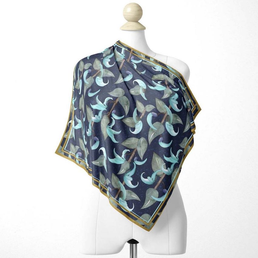 Silk scarf mockup draped over a white mannequin, featuring a blue and green botanical pattern with a gold border.