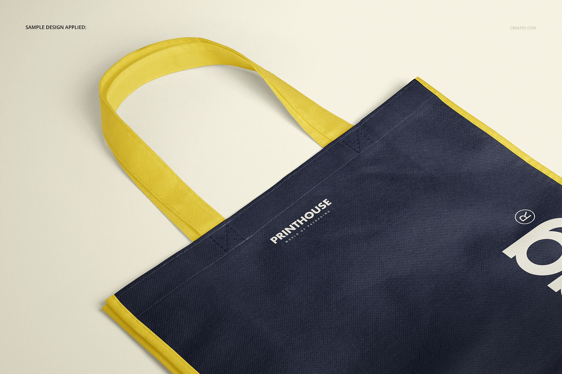Non-woven tote bag mockup with navy blue body and yellow handles, shown in a close-up angled view on a light background.