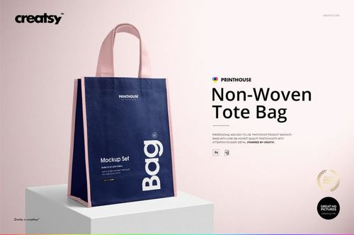 Front view of a non-woven tote bag mockup with navy blue sides and light pink handles, standing on a light surface.