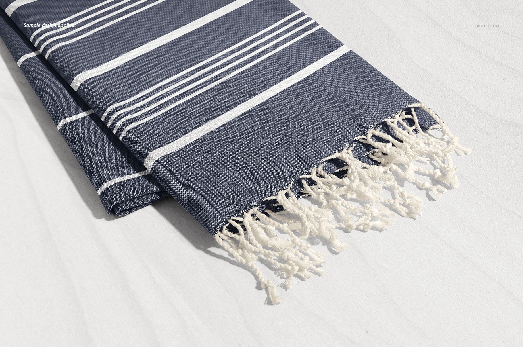 Navy blue Turkish towel mockup featuring white horizontal stripes and tassel fringe, shown from a side angle on a pale background.