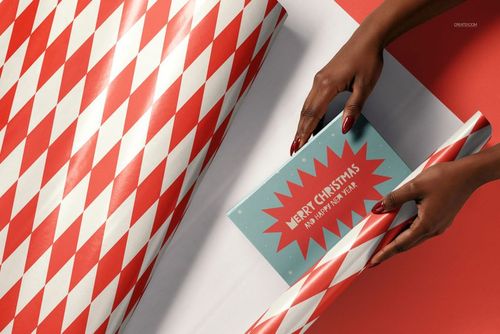 Christmas PSD mockup showing a gift being wrapped with geometric patterned paper and a greeting card nearby.