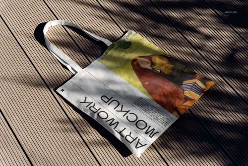 Tote bag mockup featuring a colorful design and black lettering, placed on sunlit wooden planks with soft shadows.