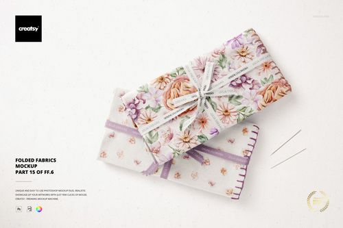 PSD mockup showing two stacked folded fabrics with purple and pink flower designs, accompanied by sewing needles.