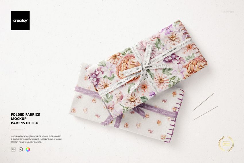 PSD mockup showing two stacked folded fabrics with purple and pink flower designs, accompanied by sewing needles.