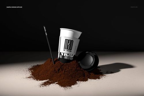 Front view of a white paper cup mockup with black sleeve and straw, partially buried in a mound of ground coffee.