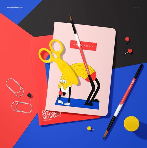 Stationery mockup with two illustrated notebooks, scissors, brushes, and office supplies arranged on vibrant surfaces.