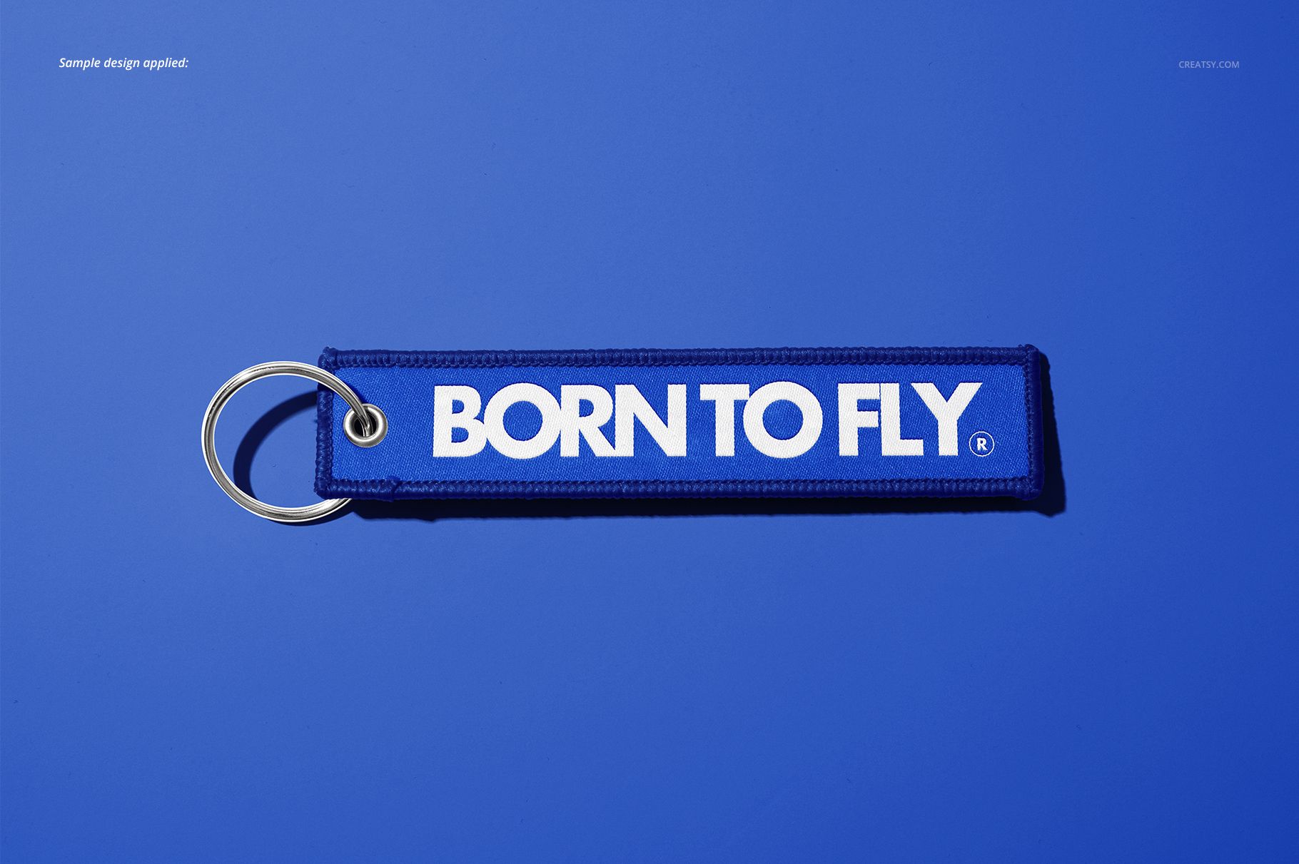 Remove Before Flight style keychain mockup featuring a blue fabric tag and silver key ring on a blue surface.