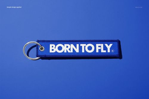 Remove Before Flight style keychain mockup featuring a blue fabric tag and silver key ring on a blue surface.
